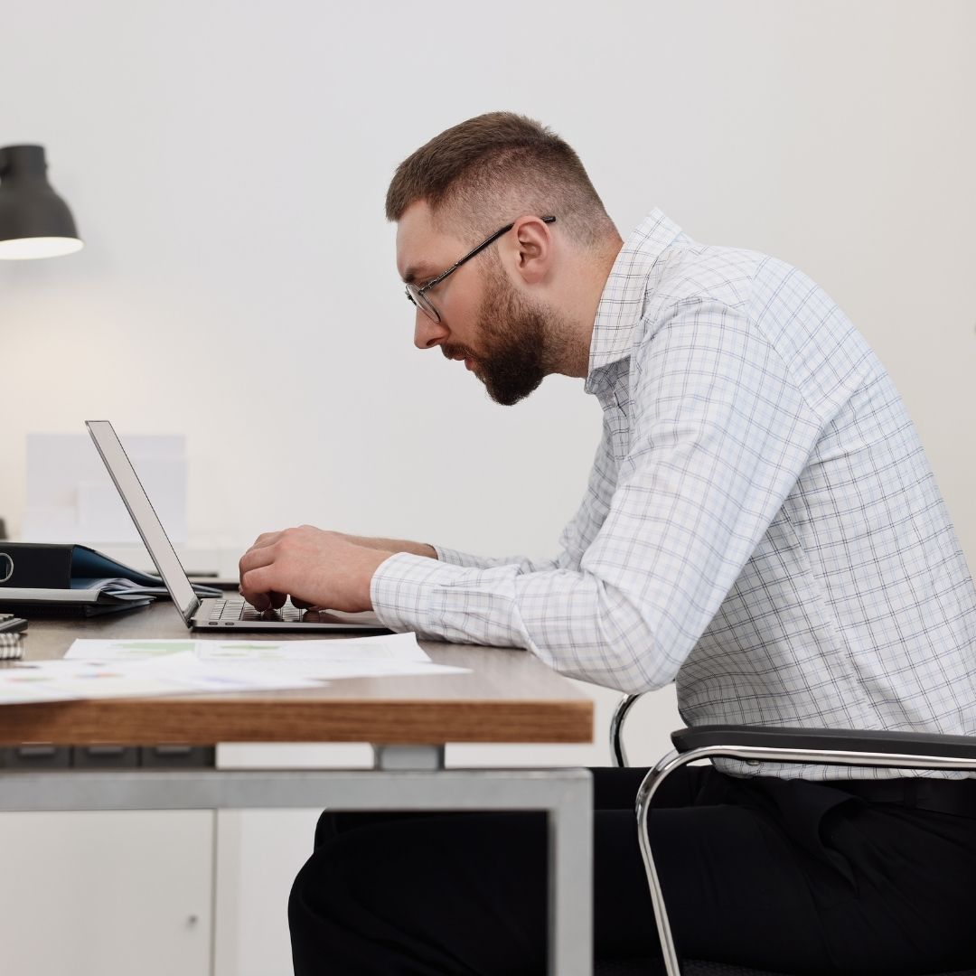 Person leaning forward at a desk, working on a laptop with charts and documents spread out.