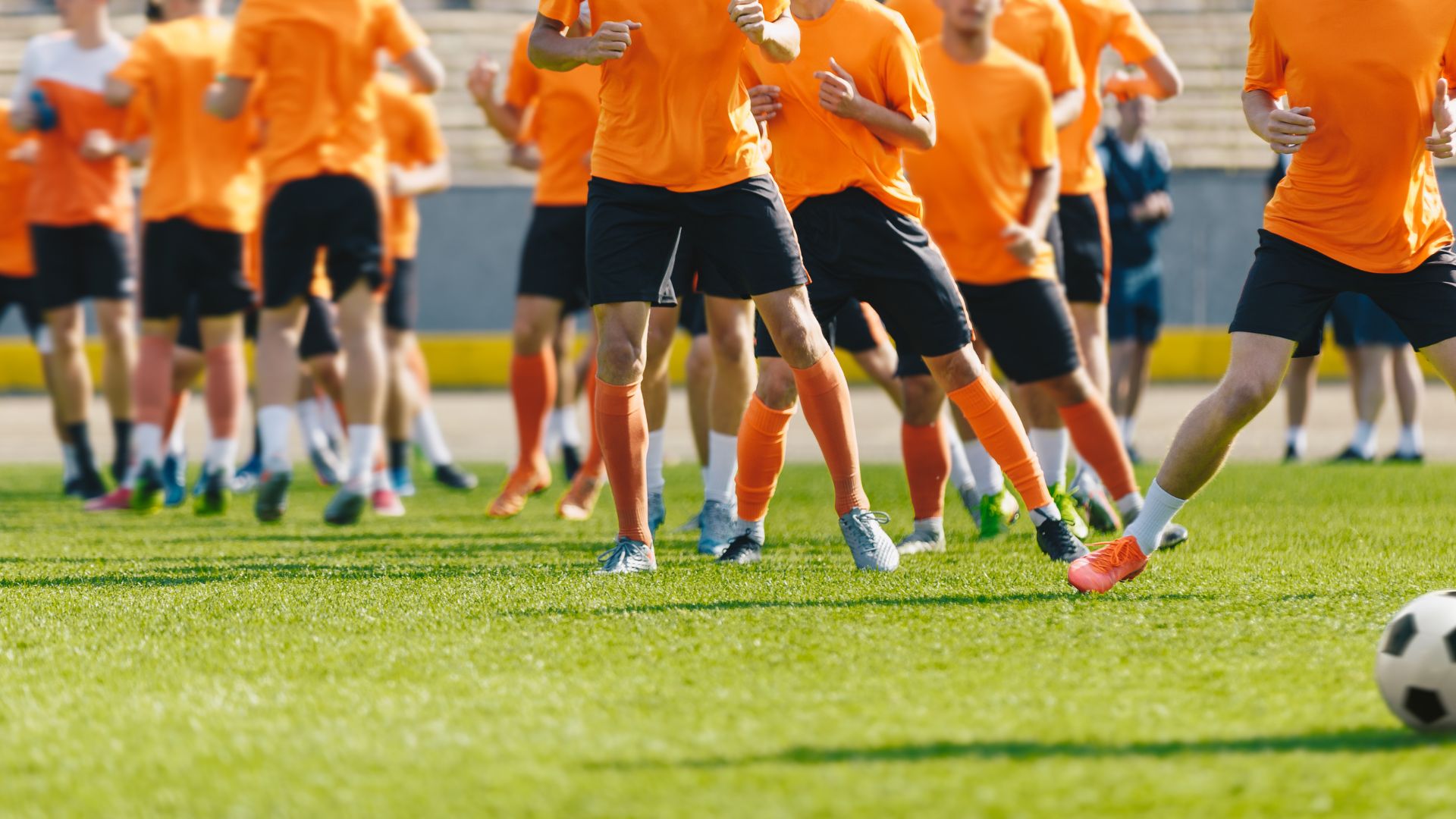School Athletics Soccer players in orange jerseys warming up on a grass field, with one player preparing to kick the ball.