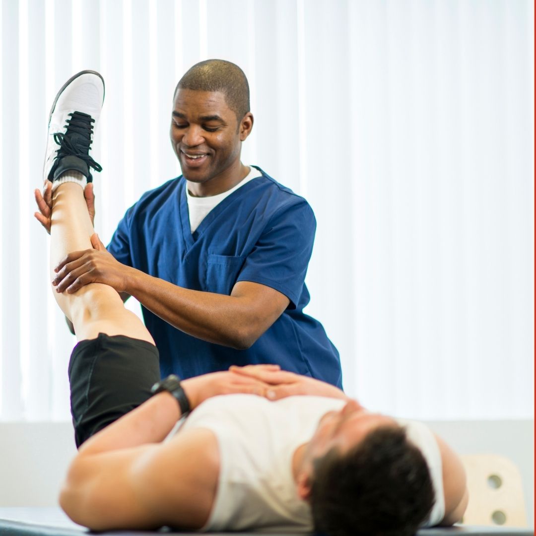 Physical therapist in blue scrubs stretching a patient’s leg during rehabilitation on a treatment table.